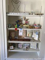 Full view of four shelves filled with assorted novelty decor and art items, including signs, figurines, frames, and small baskets.
