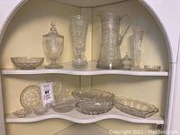 Shelf display of assorted crystal and glass serving and decorative items including pitchers, vases, bowls, and dishes.