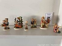 Photo showing all six Hummel figurines in a row on a flat surface.