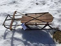 Side view of the full sled on snow showing wooden seat slats and metal steering bar, vintage condition.
