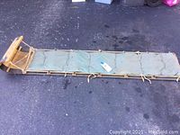 Full view of the 7-foot wood toboggan with a green tufted cushion tied on the top, showing its length and rope attachment at front.