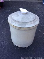 Full view of off-white 5 gallon ceramic crock with matching lid on outdoor surface.