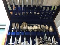 Full view of mixed sterling and community plate flatware in blue velvet-lined wooden case showing forks, spoons, and knives.