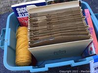 Photo of blue plastic bin containing vintage knitting pattern booklets in brown envelopes, two skeins of yellow yarn, and other books including a sign language book and a Christmas book.