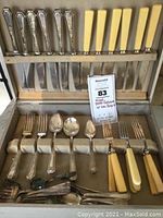 Photo showing open wooden case with slots containing a mixed lot of Wm Rogers silverplate flatware including knives with ivory-colored handles and various forks and spoons.