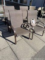 Four brown outdoor deck chairs arranged on a patio, showing front and side views with armrests and woven seats.