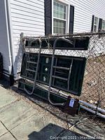 Folded picnic table leaning against a chain link fence showing the entire table folded flat and metal frame.