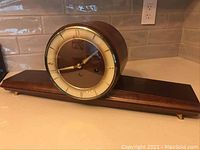 Side view of vintage mantle clock showing wooden base and round dial with glass cover closed