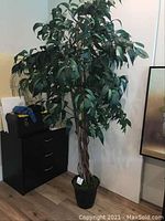 Full view of artificial tall tree plant with thick green foliage and twisted wood trunk in black pot