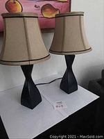 Photo of two table lamps unlit on a white surface against a wall with fruit artwork above.