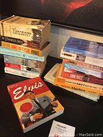 Stack of multiple mixed books including fiction and biography titles arranged on dark surface