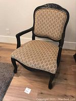 Photo showing front view of the Louis inspired armchair with upholstered seat and backrest, black frame and carved details on legs and top of backrest.