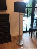 Full view of the floor lamp showing the black shade and brushed chrome base.
