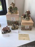 Four miniature David Winter cottages displayed on a table with original boxes and certificate of authenticity.