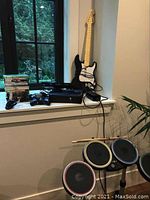 Overall view of console on windowsill with wired controllers, guitar, drums and games