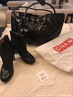 Nine West black patent handbag with drawstring and two handles, black leather boots, and white bag with red Nine West logo.