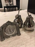 Photo showing Seagull clock and two silver-tone decorative pears on a beige fabric surface.