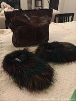 Photo showing brown leather handbag with two front pockets and a zippered side pocket alongside colorful fur slippers.