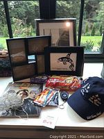 Photo showing multiple picture frames including one with a Skahna orca print, a Hunger Games illustrated book, hand warmers, string fairy lights, and a navy blue Disney cap with Mickey Mouse.