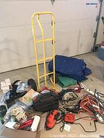 Overview of the entire lot showing the yellow hand truck dolly, assorted tools including circular saws, sander, drill, cords and other accessories laid on the floor.