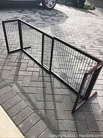 Photo of the expandable wooden and wire mesh barrier fence expanded partially, placed on an outdoor paved surface.
