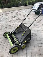 Front view of the Sunjoe push lawn mower showing the blades and attached black grass collector bag with yellow clips.