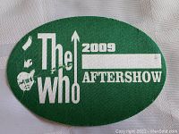 Oval green fabric backstage pass with white text and guitar silhouette, marked "The Who 2009 AFTERSHOW" with blank insertion area.
