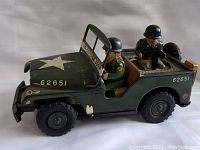 Side view of the olive green tin military jeep showing one soldier figure in the driver's seat and another behind a mounted machine gun.