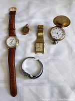 Top-down photo showing all five watches on a fabric surface, including wristwatches and pocket watches.
