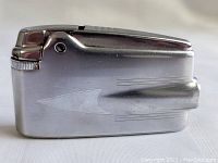 Side angle view of vintage Ronson Varaflame pocket lighter showing brushed metal finish with etched arrow and geometric Art Deco motifs.
