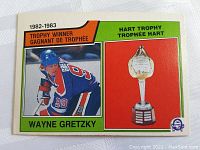Front of 1983-84 OPC hockey card showing Wayne Gretzky in Edmonton Oilers uniform and Hart Trophy illustration.