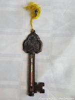 Front view of the vintage Ohio key-shaped thermometer showing embossed details and thermometer tube, hanging by yellow cord.