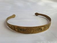 Full view of narrow brass cuff bracelet revealing engraved floral and geometric designs along the band.