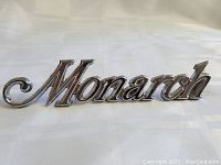 Close-up photo of the 'Monarch' emblem showing the shiny chrome finish and script style lettering.