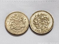 Two British one pound coins showing reverse side designs. One coin has the British coat of arms with lion and unicorn; the other has three lions passant guardant marking old English heraldic emblem.