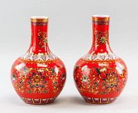 Pair of red porcelain vases with tall necks, globular bodies, and floral designs on a white background.