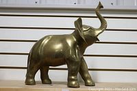 Front right angle of the large brass elephant statue showcasing full side view and raised trunk
