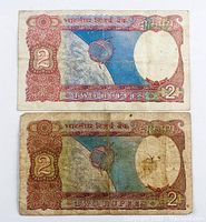 Front side of two 1976 Indian 2 Rupees banknotes showing satellite over earth design, denomination, and intricate floral patterns.