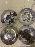 Four round collectable plates with various rural and snowy scenes, all signed and numbered