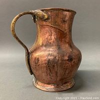 Full view of the primitive hand hammered copper pitcher showing rounded body, spout, and base.