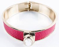 Close-up of the bangle showing gold-tone metal frame with textured dark pink band and round Swarovski crystal at clasp.