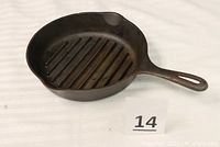 Top angle showing cast iron grill pan with flat bottom and ridged cooking surface, including handle with elongated hole.