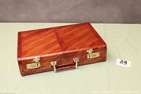 Closed brown eelskin briefcase showing exterior, handle, and two gold-toned combination locks on front.