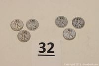 Six Walking Liberty half dollar coins laid out on a beige surface, showing usual wear and tarnish for circulated coins.