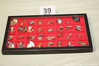 Front view of black framed glass showcase with 32 red square compartments filled with assorted pins of various themes and styles.