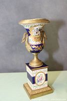 Full view of the urn showing the shape, swan head handles, and square base with floral painted decoration.