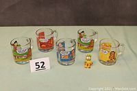Five clear glass mugs with Garfield and Odie cartoons and one small Garfield figurine.