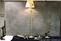 Full view of the floor lamp, fireplace tool set, eagle, and carriage light base displayed on a table against a grey background.