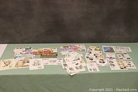 Wide shot of multiple USA first day covers and stamp boards arranged on table, showing variety of themes and postmarks.