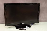 Full front view of Panasonic Viera 37 inch LCD TV showing black bezel and screen off. Remote control lying in front.